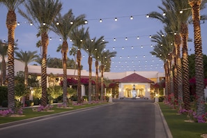 A hotel entrance with palm trees, string lights, and a well-maintained lawn. - The Scottsdale Resort and Spa, Curio Collection by Hilton (Scottsdale)