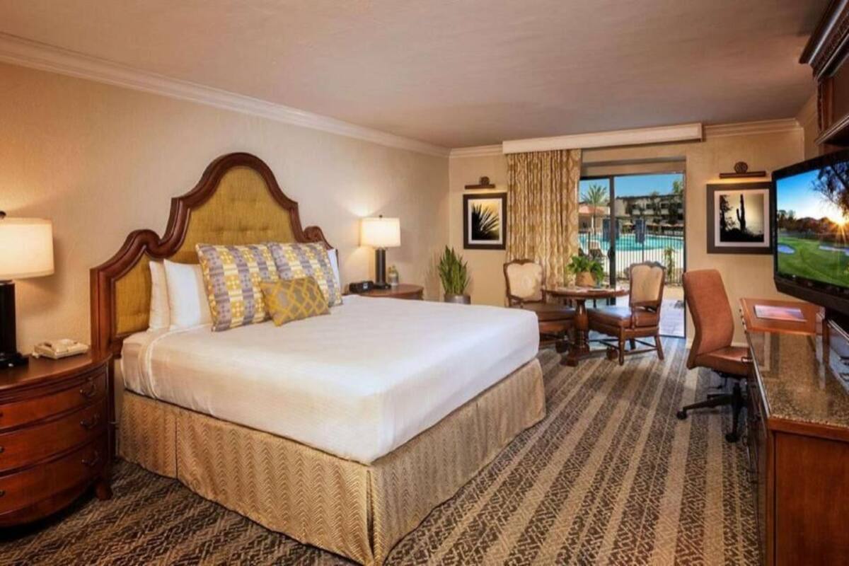 A hotel room with a large bed, a desk, a television, and a view of a golf course.
