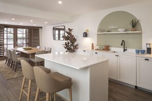 A modern kitchen with a central island, bar stools, a dining area with chairs, and a large window with blinds. - The Scottsdale Resort and Spa, Curio Collection by Hilton (Scottsdale)