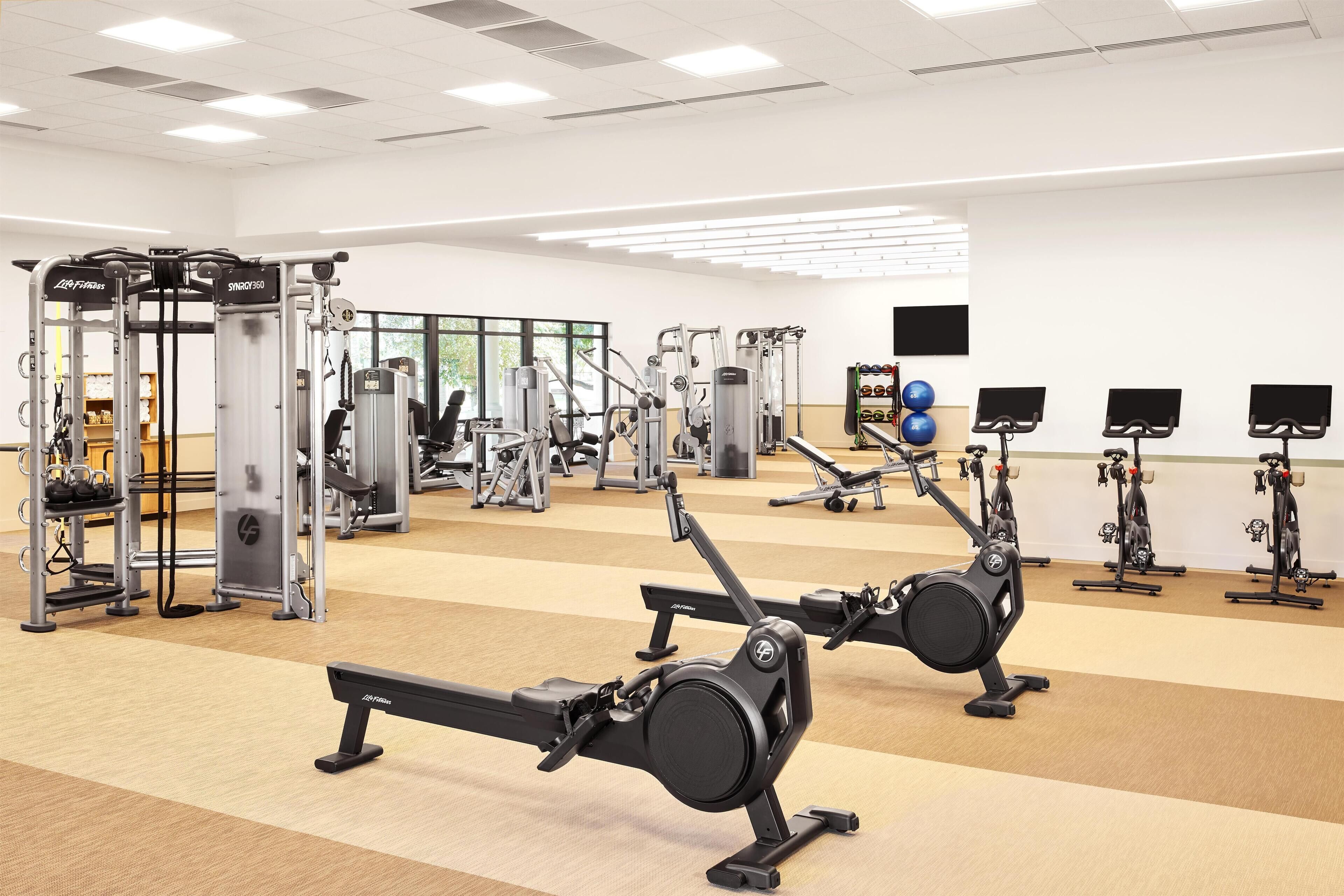 Un gimnasio con máquinas de cardio, equipo de levantamiento de pesas y espejos en las paredes.