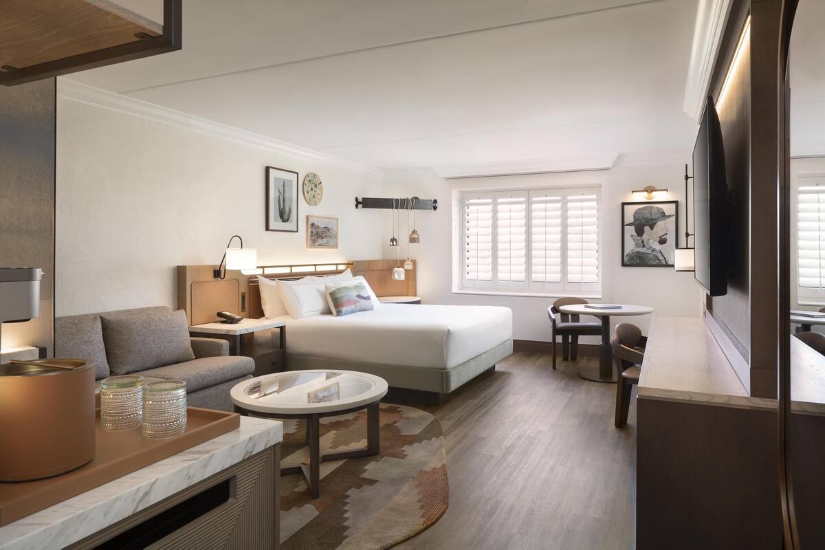 A modern hotel room with a bed, sofa, round dining table, and a TV.
