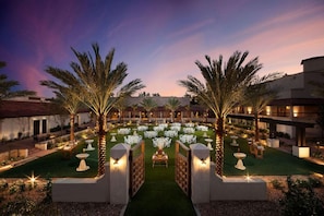 A courtyard with a central dining area, surrounded by palm trees and illuminated by ambient lighting. - The Scottsdale Resort and Spa, Curio Collection by Hilton (Scottsdale)