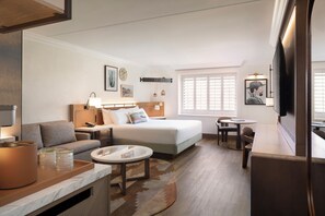 A hotel room with a bed, a sofa, a desk, a TV, and a window with blinds. - The Scottsdale Resort and Spa, Curio Collection by Hilton (Scottsdale)