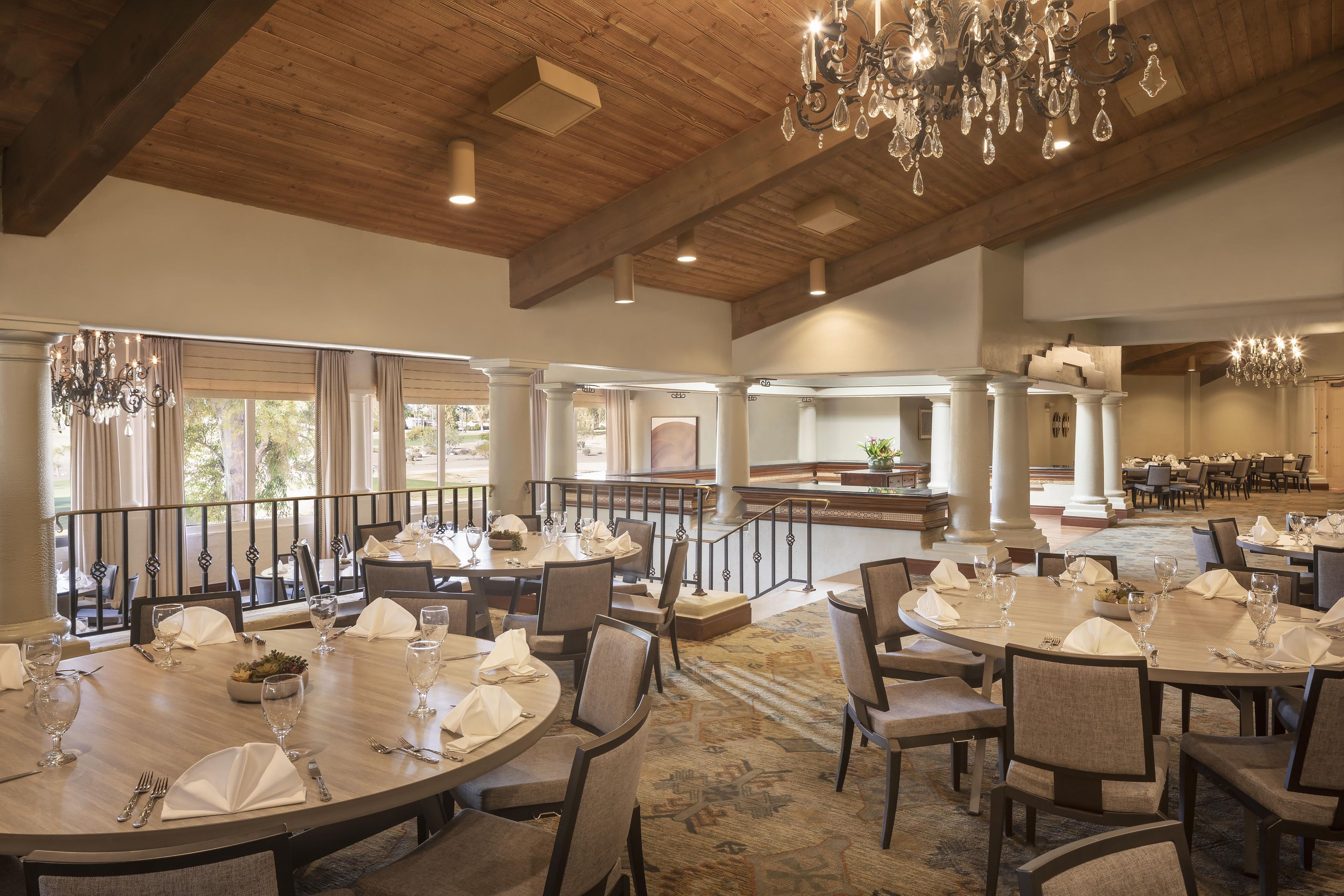 A spacious dining area with round tables, chairs, and chandeliers.