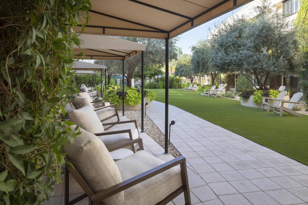 A covered outdoor seating area with chairs and a lawn.
