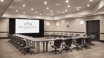A conference room with a long table, chairs, a projector screen, and a logo for The Scottsdale Resort & Spa.