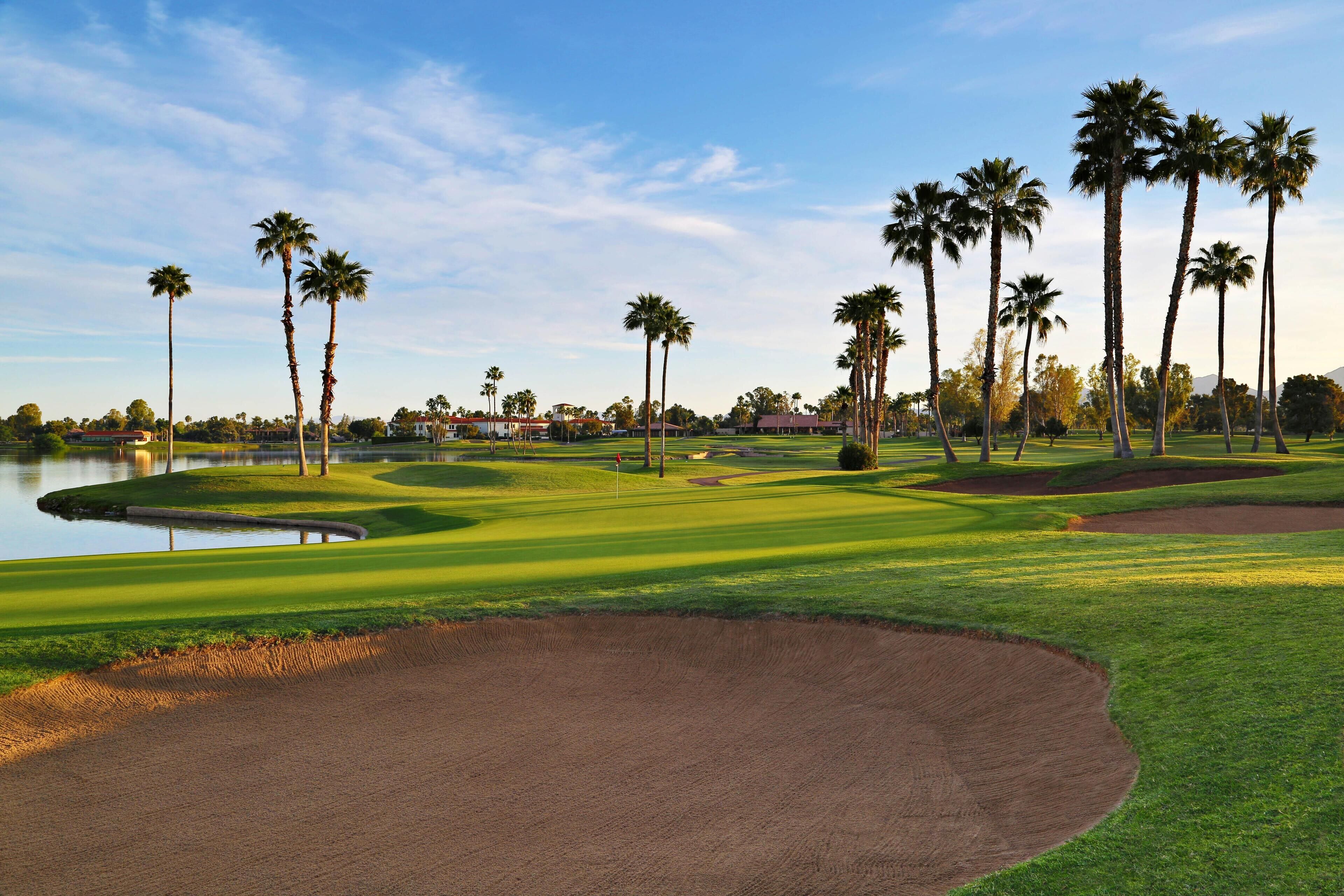 Campo de golf con bunkers de arena, palmeras y una masa de agua.