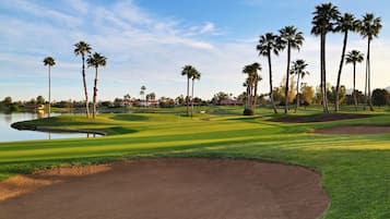 Campo de golf con bunkers de arena, palmeras y una masa de agua.