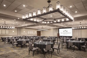 A conference room with multiple tables and chairs, a large screen displaying 'The Scottsdale Resort & Spa', and a sophisticated chandelier. - The Scottsdale Resort and Spa, Curio Collection by Hilton (Scottsdale)