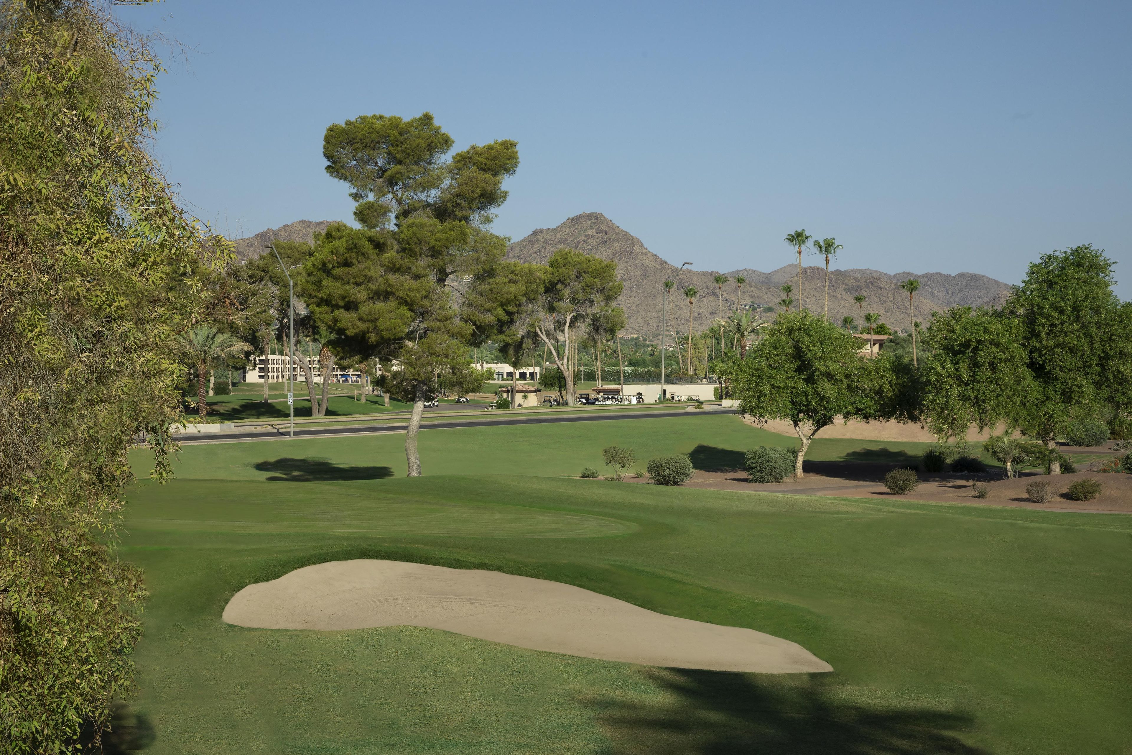 Un campo de golf con un búnker de arena, árboles y una montaña al fondo.