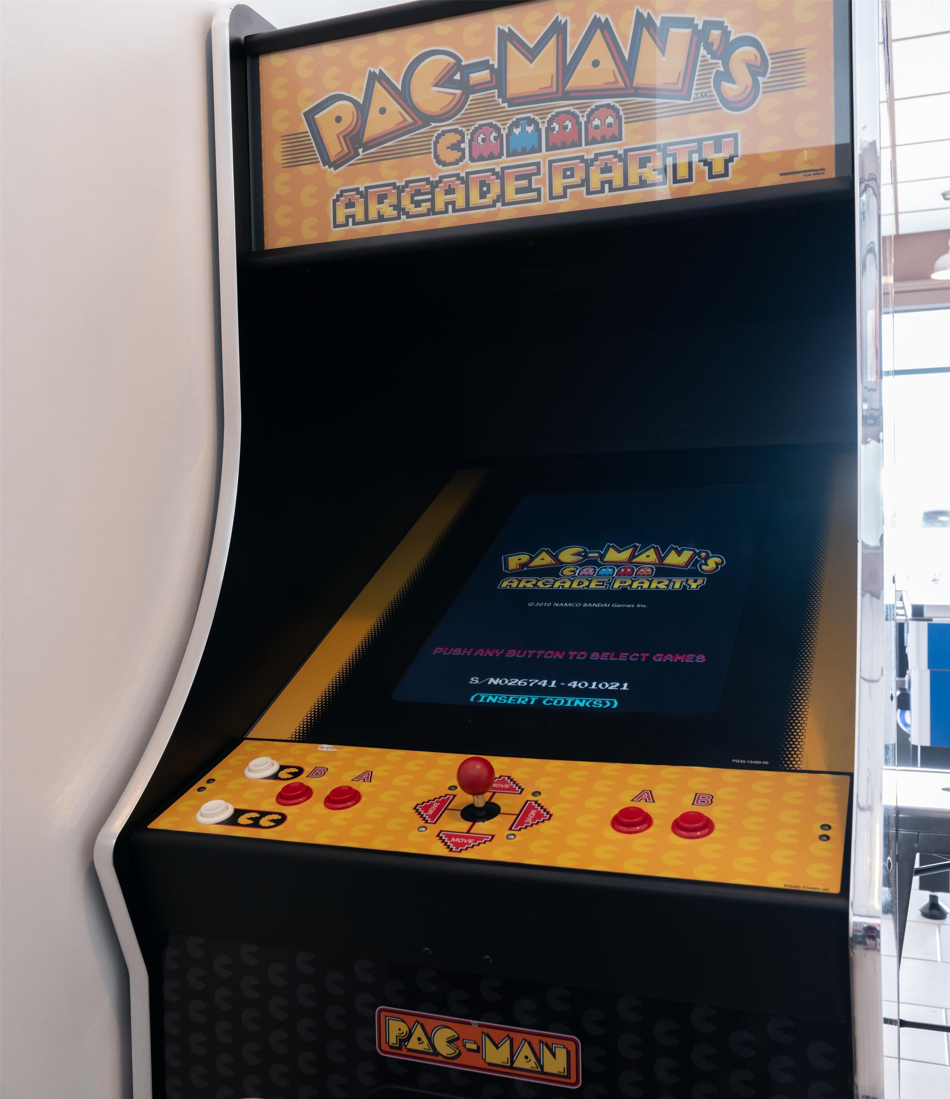Une borne d’arcade Pac-Man avec un panneau en bois et un écran affichant les instructions du jeu.