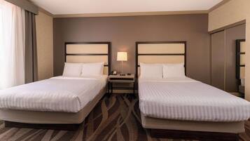 Habitación de hotel con dos camas, una mesita de noche, una lámpara y un ventanal con cortinas.