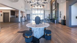 Un vaste espace de vie agrémenté d’une table basse en marbre, de tabourets rembourrés bleus et d’un lustre moderne.
