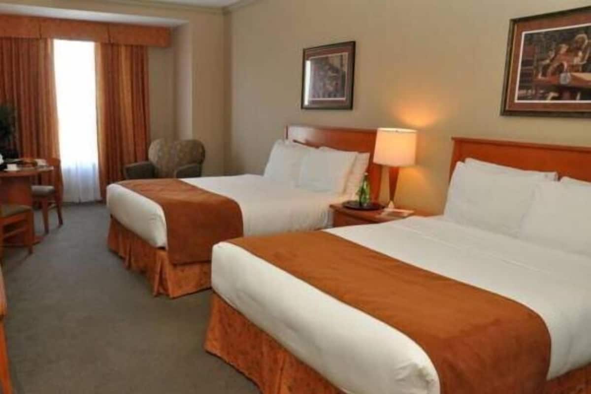 A hotel room with two beds, a desk, a chair, a lamp, and two framed pictures on the wall.