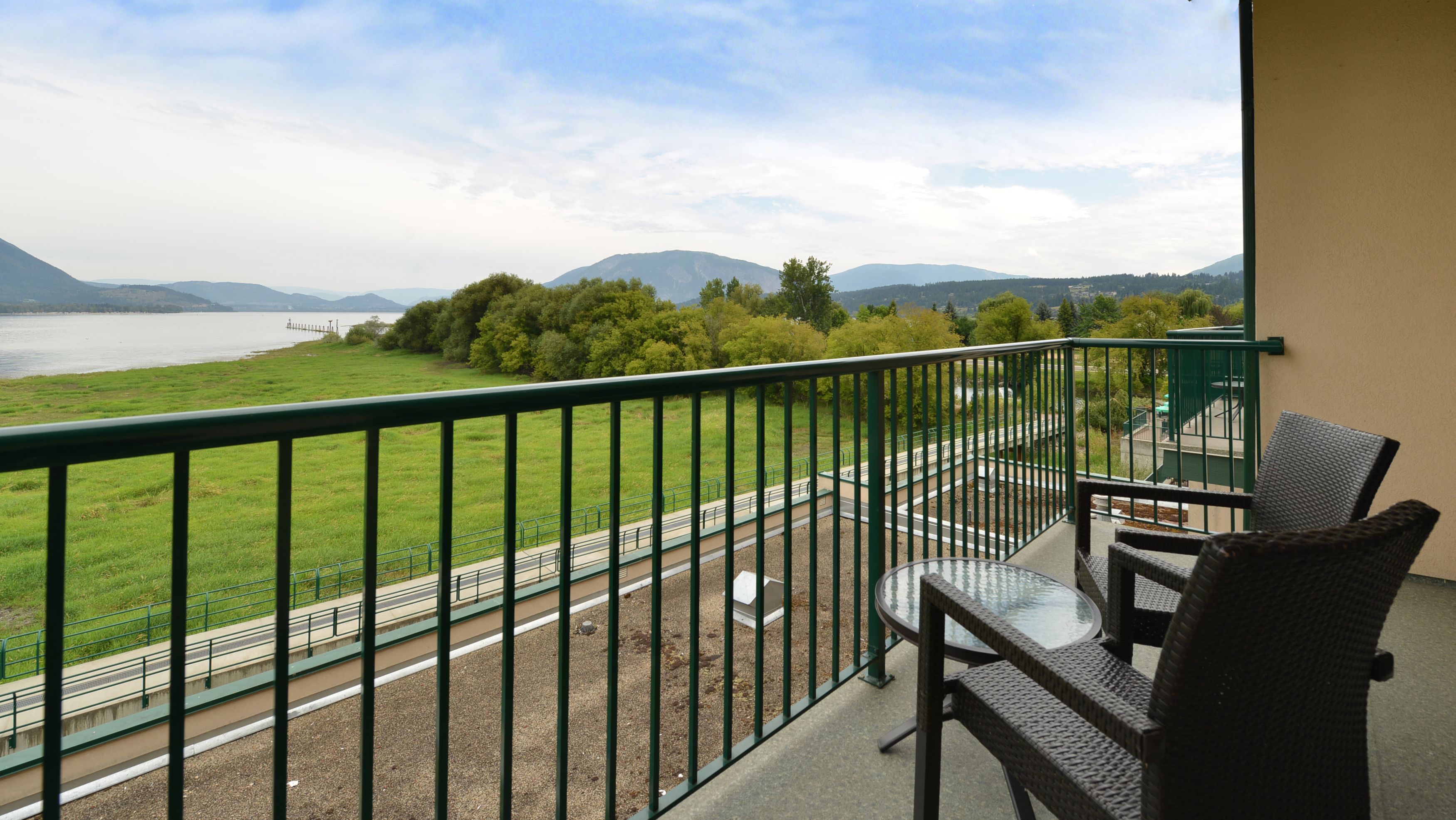 A balcony with a view of a lake, a road, and distant mountains.