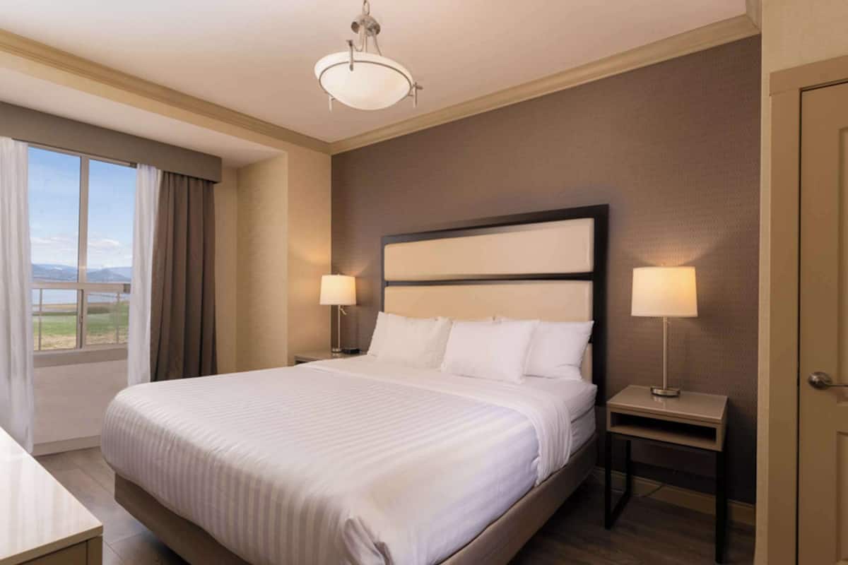 A hotel room with a large bed, two bedside lamps, a nightstand, a desk, and a door.