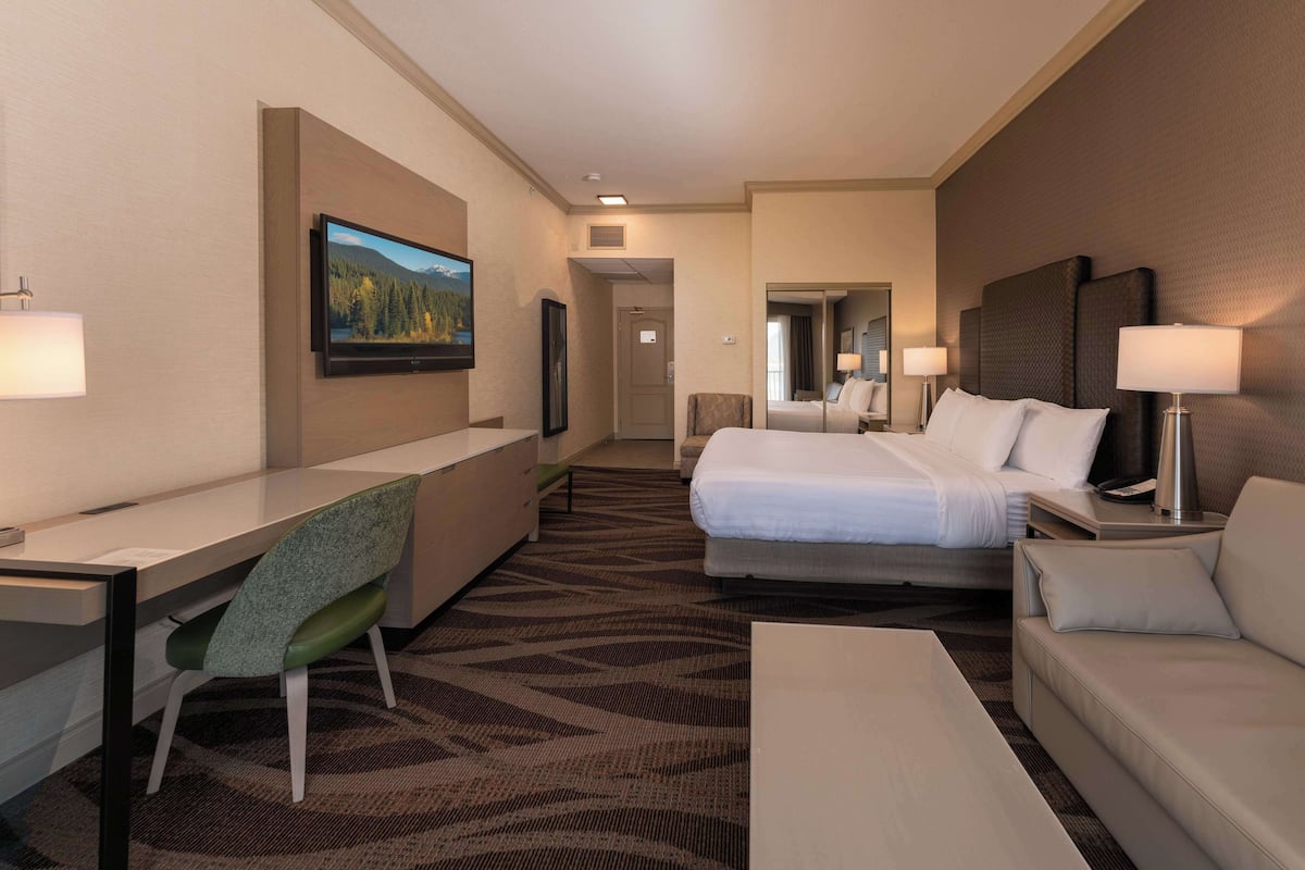 A hotel room with a bed, a desk, a chair, a sofa, and a TV.