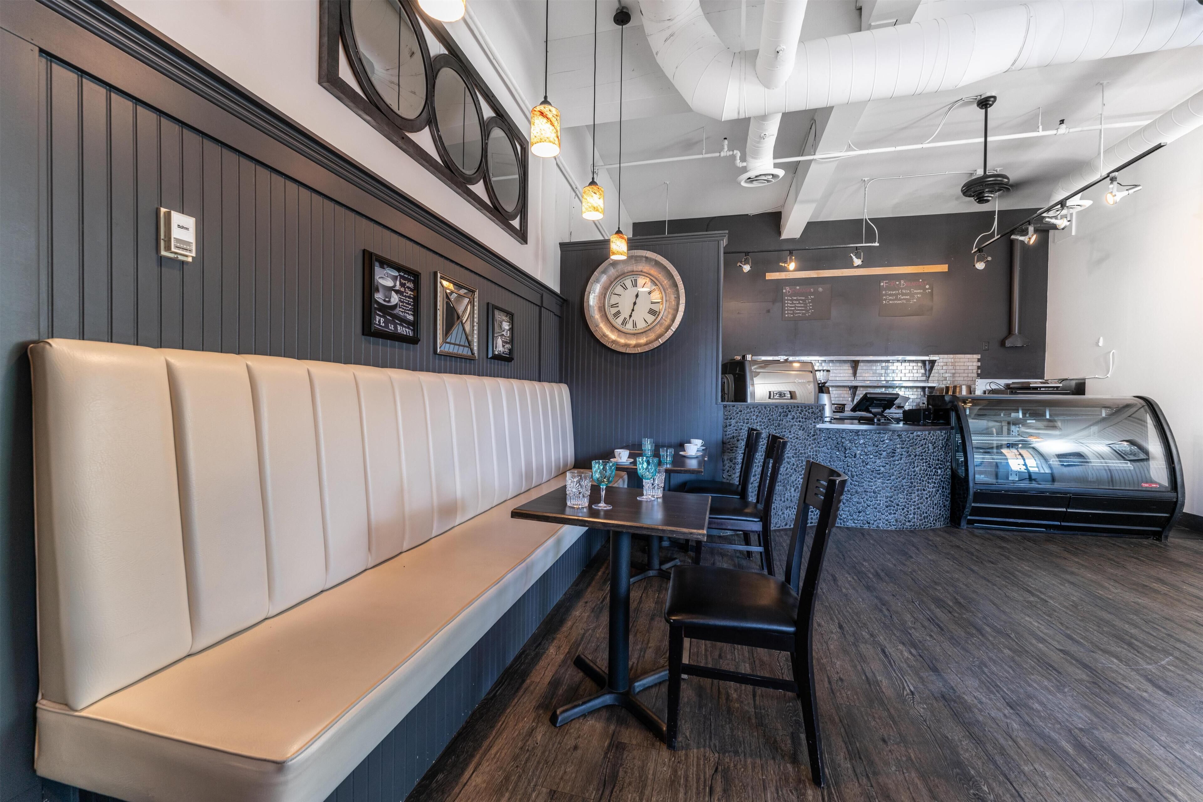 A restaurant interior with a booth seating area, a round wall clock, and a counter with a display case.