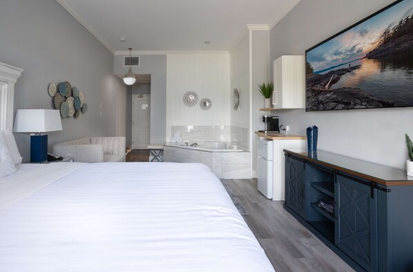 Una habitación de hotel moderna con una cama grande, un baño con bañera y un comedor con vistas al agua.