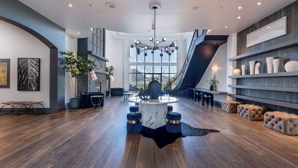 Un intérieur spacieux et moderne, avec une table centrale en marbre, des sièges rembourrés en tissu bleu et un escalier menant à un niveau supérieur.