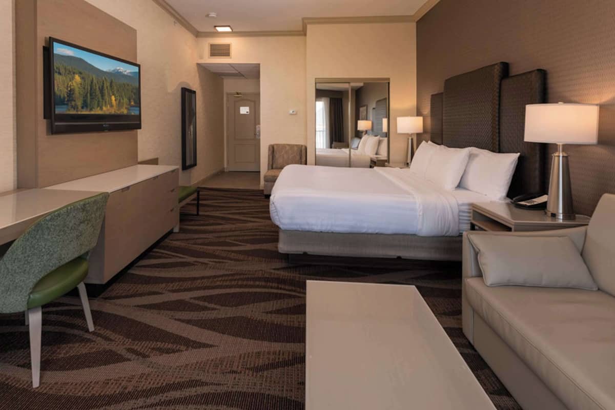 A hotel room with a bed, a desk, a chair, a sofa, and a TV.