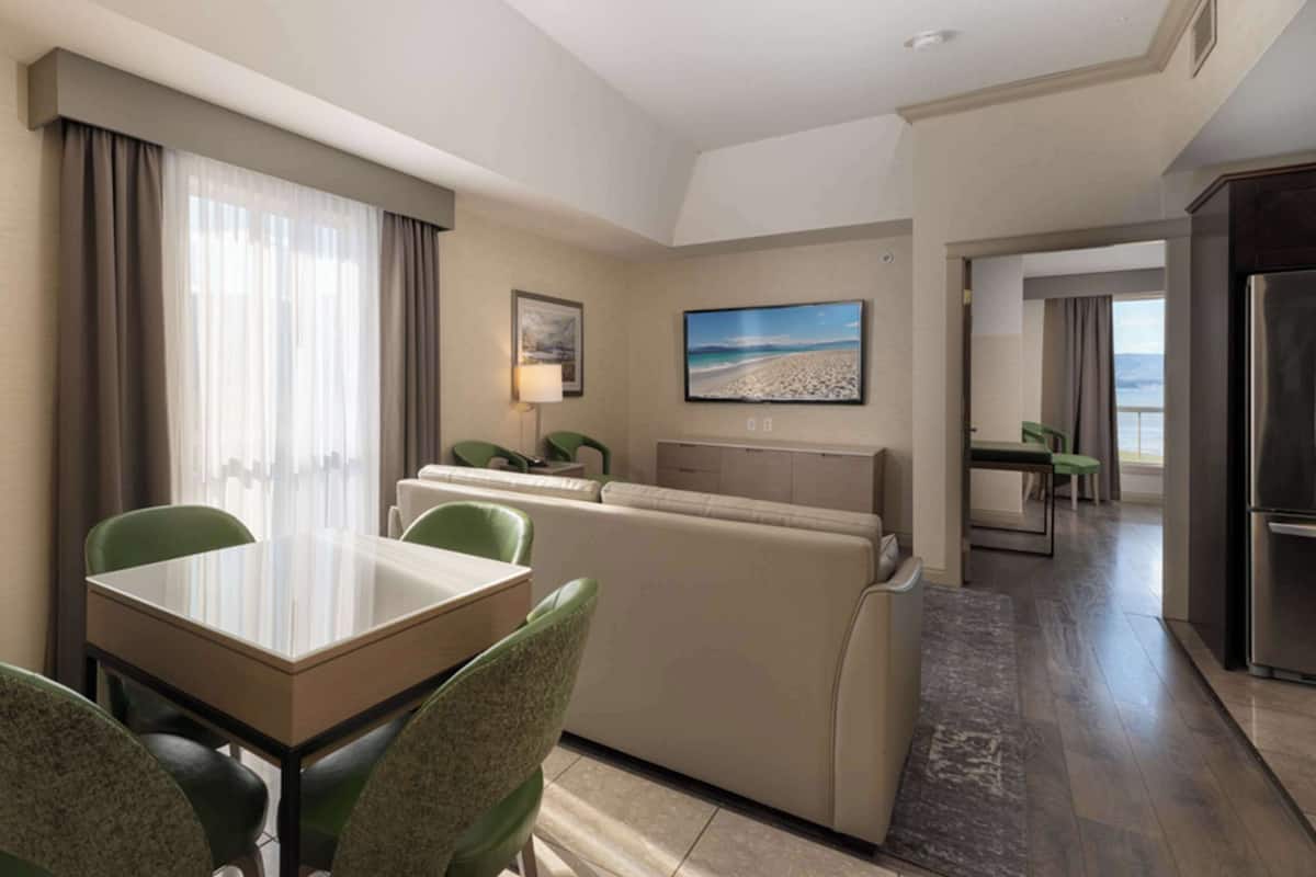 A hotel room with a dining area, a sofa, a TV, and a view of the beach.