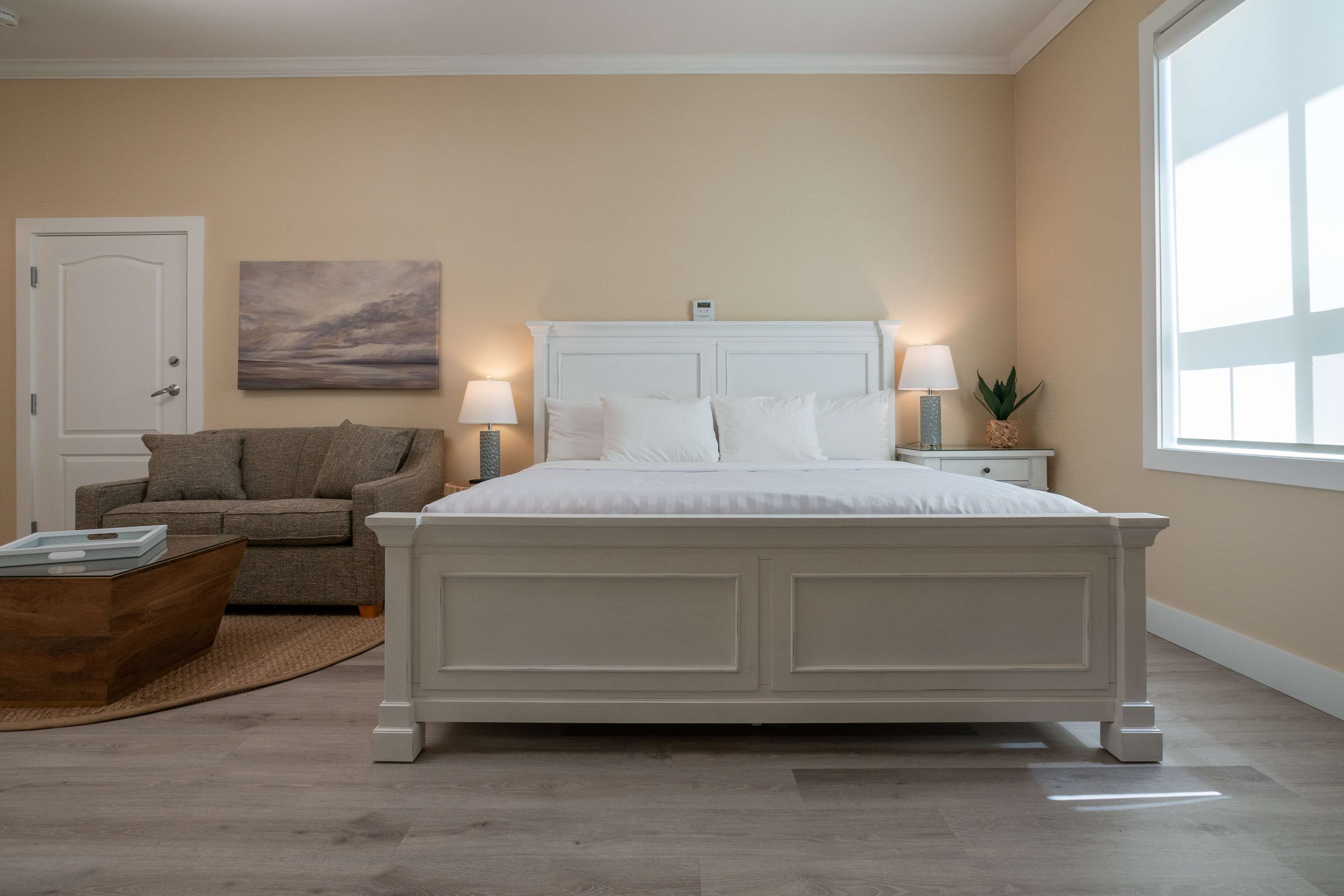 A bedroom with a large bed, a sofa, a coffee table, and a painting on the wall.