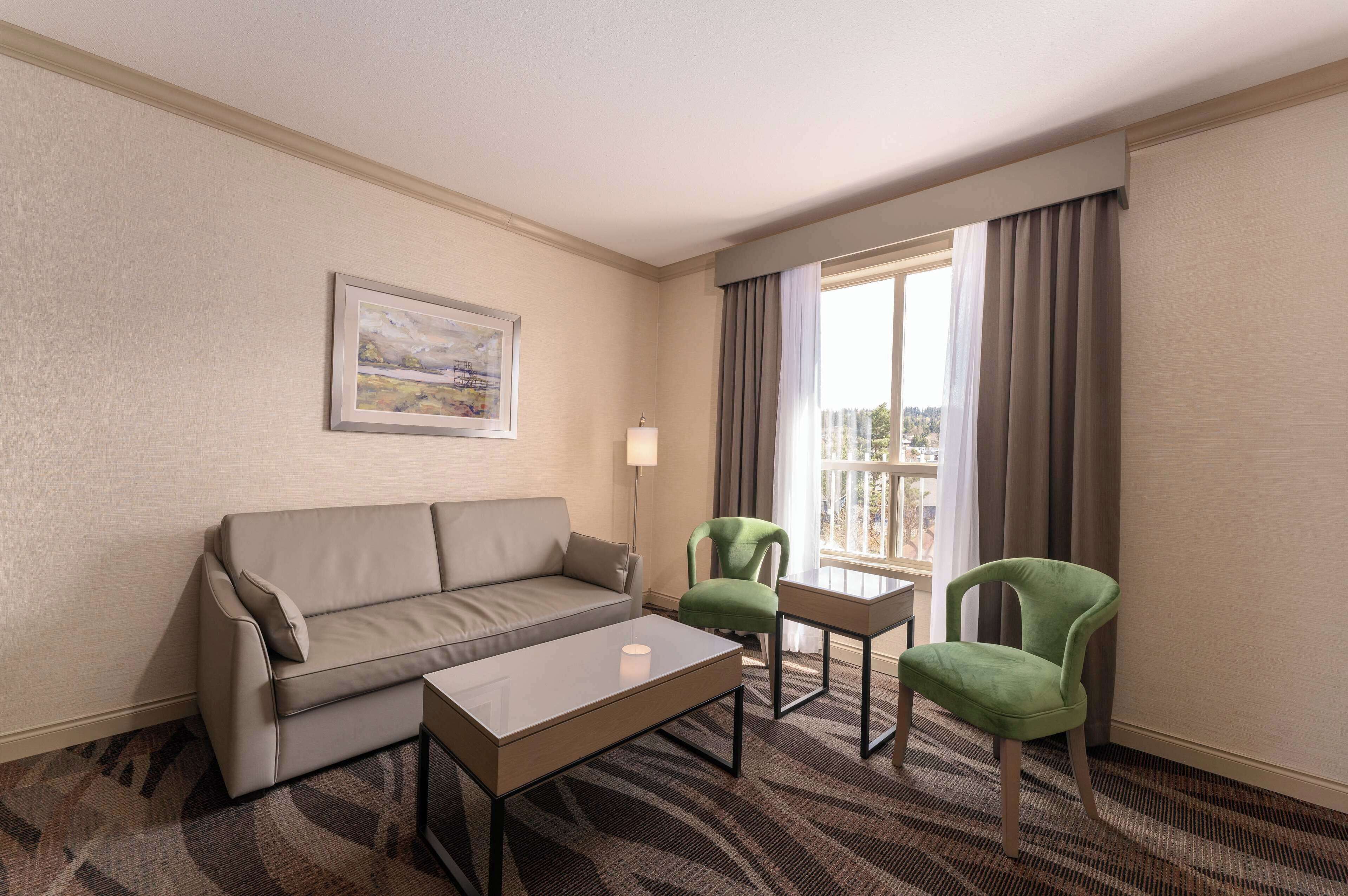 Une chambre d’hôtel avec un canapé, deux fauteuils, une petite table, une lampe et une fenêtre avec des rideaux.