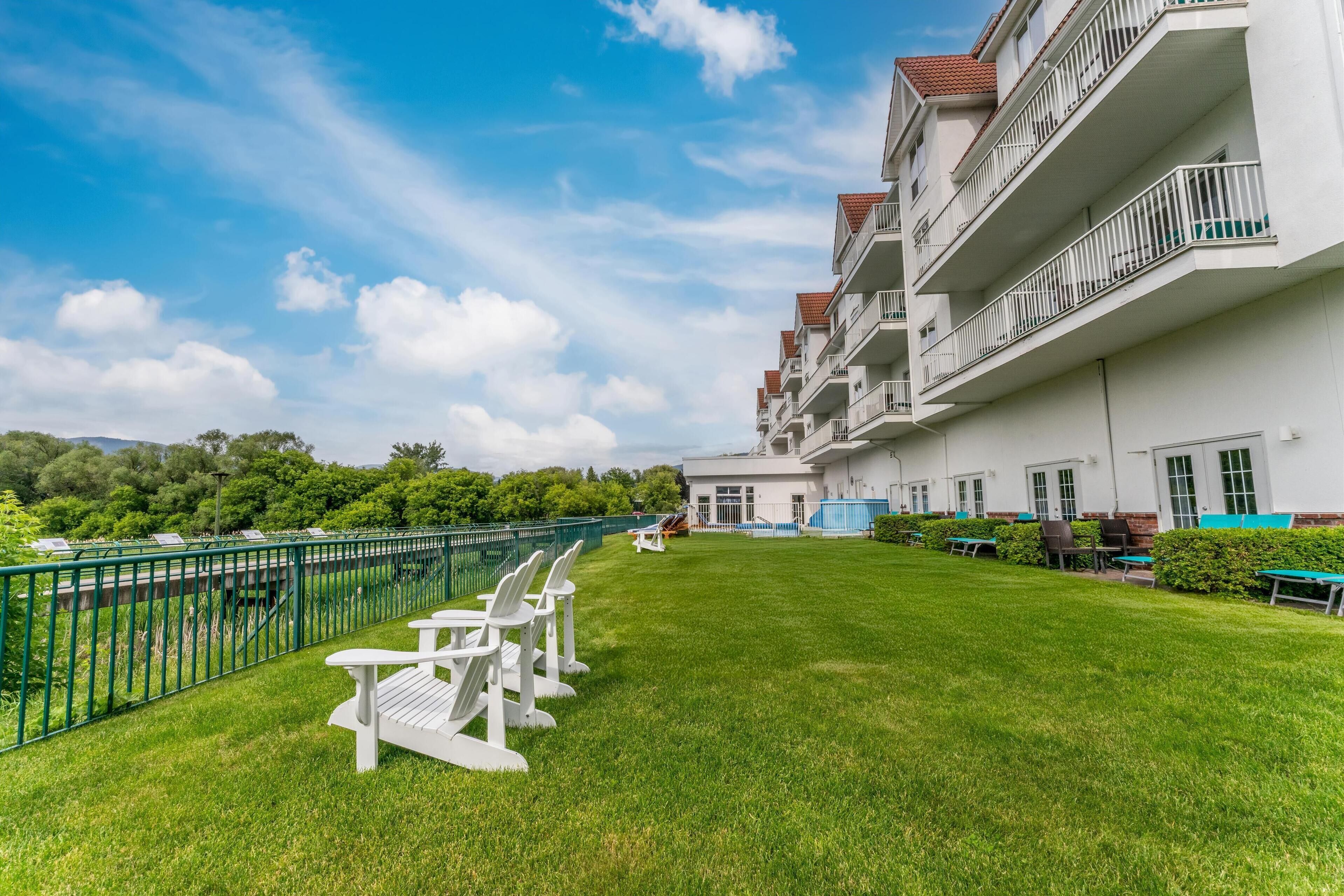 A hotel with a well-maintained lawn, outdoor seating area with tables and chairs, and a balcony with railings.