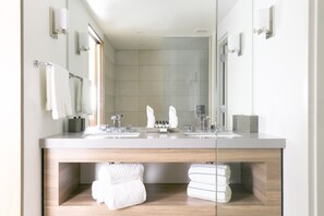 A modern bathroom with a large mirror, two sinks, and a wooden vanity.