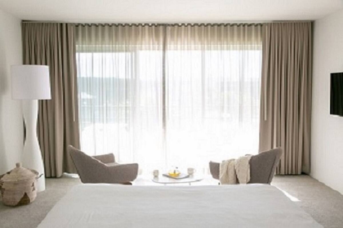A hotel room with a large bed, two armchairs, a coffee table, and a view through sheer curtains.
