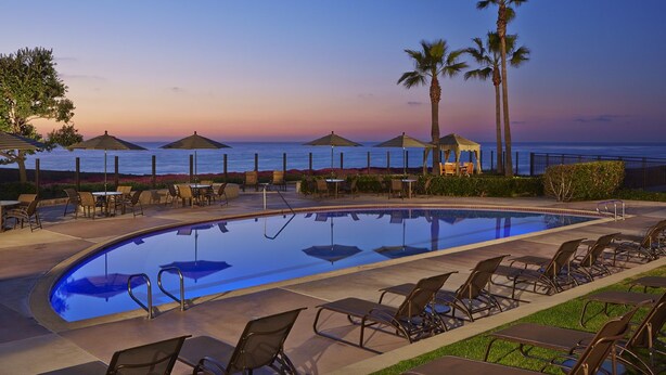 A poolside area with lounge chairs, umbrellas, and a view of the ocean at sunset. - Carlsbad Seapointe Resort (Carlsbad)