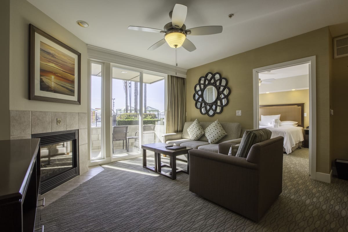 A spacious living area with a fireplace, a ceiling fan, a large mirror, and a balcony with a view.