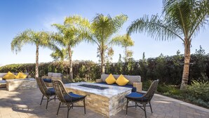An outdoor patio with a stone fire feature, wicker chairs, and a sofa with yellow cushions. - Carlsbad Seapointe Resort (Carlsbad)