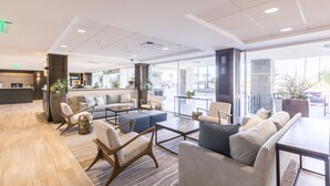 A modern lobby with a reception desk, seating area with sofas and chairs, and large windows offering views of the outdoors. - Carlsbad Seapointe Resort (Carlsbad)