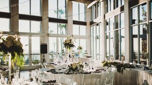 A spacious indoor venue with large windows, tables set for dining, and decorative floral arrangements. - Carlsbad Seapointe Resort (Carlsbad)