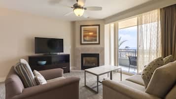 Un salón con sofá, sillón, televisor, chimenea y un balcón con vistas.