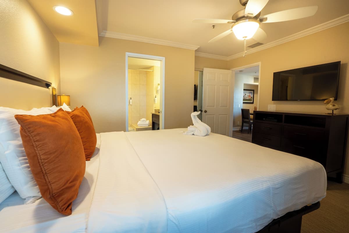 A hotel room with a large bed, a ceiling fan, a flat-screen TV, and a desk with a chair.