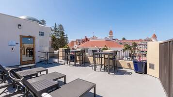 A rooftop terrace with lounge chairs and tables, a door, and a view of a historic building with a red roof.