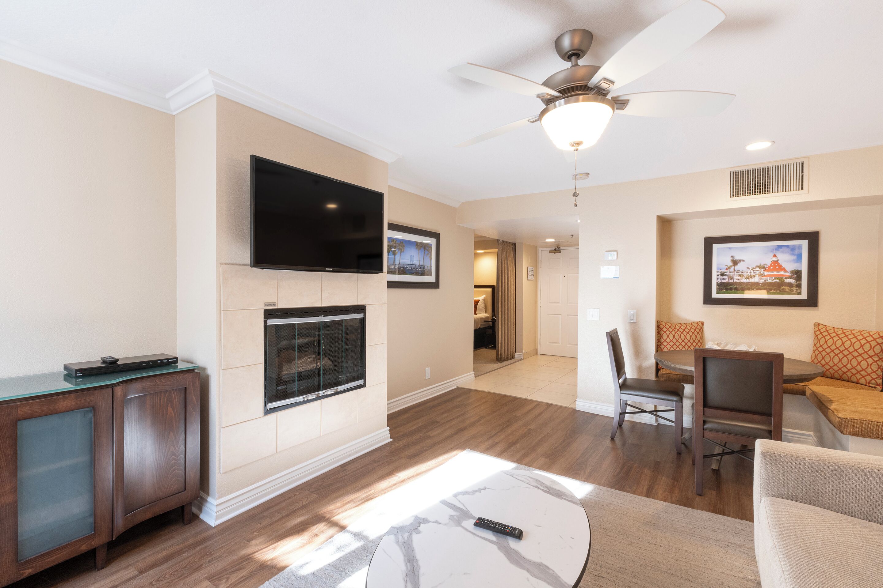 A modern living room with a flat-screen TV, fireplace, ceiling fan, and a dining area with a table and chairs.