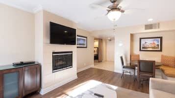 A modern living room with a flat-screen TV, fireplace, ceiling fan, and a dining area with a table and chairs.