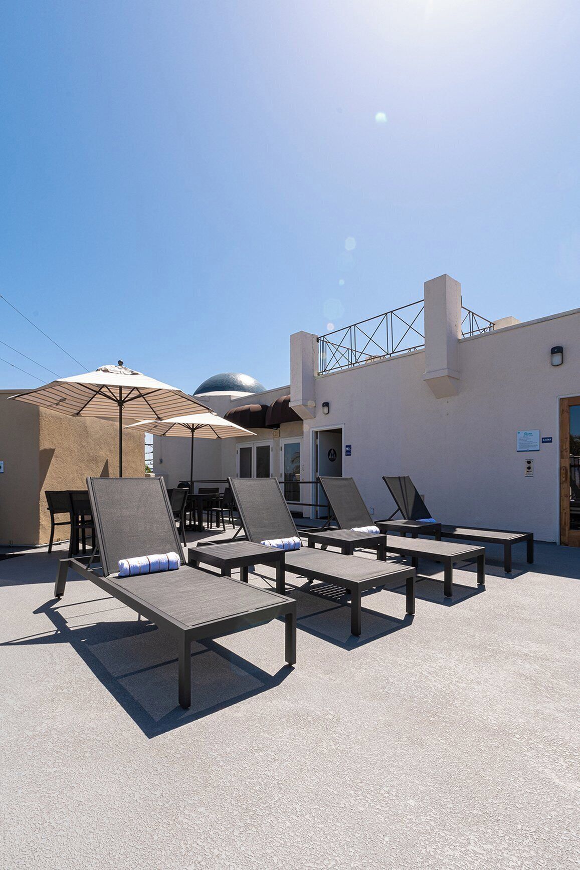 An outdoor lounge area with sun loungers and umbrellas, a pool, and a building with a dome and a staircase.