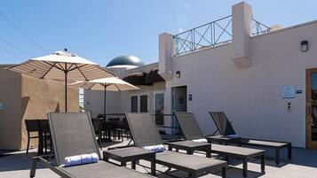 An outdoor lounge area with sun loungers and umbrellas, a pool, and a building with a dome and a staircase.