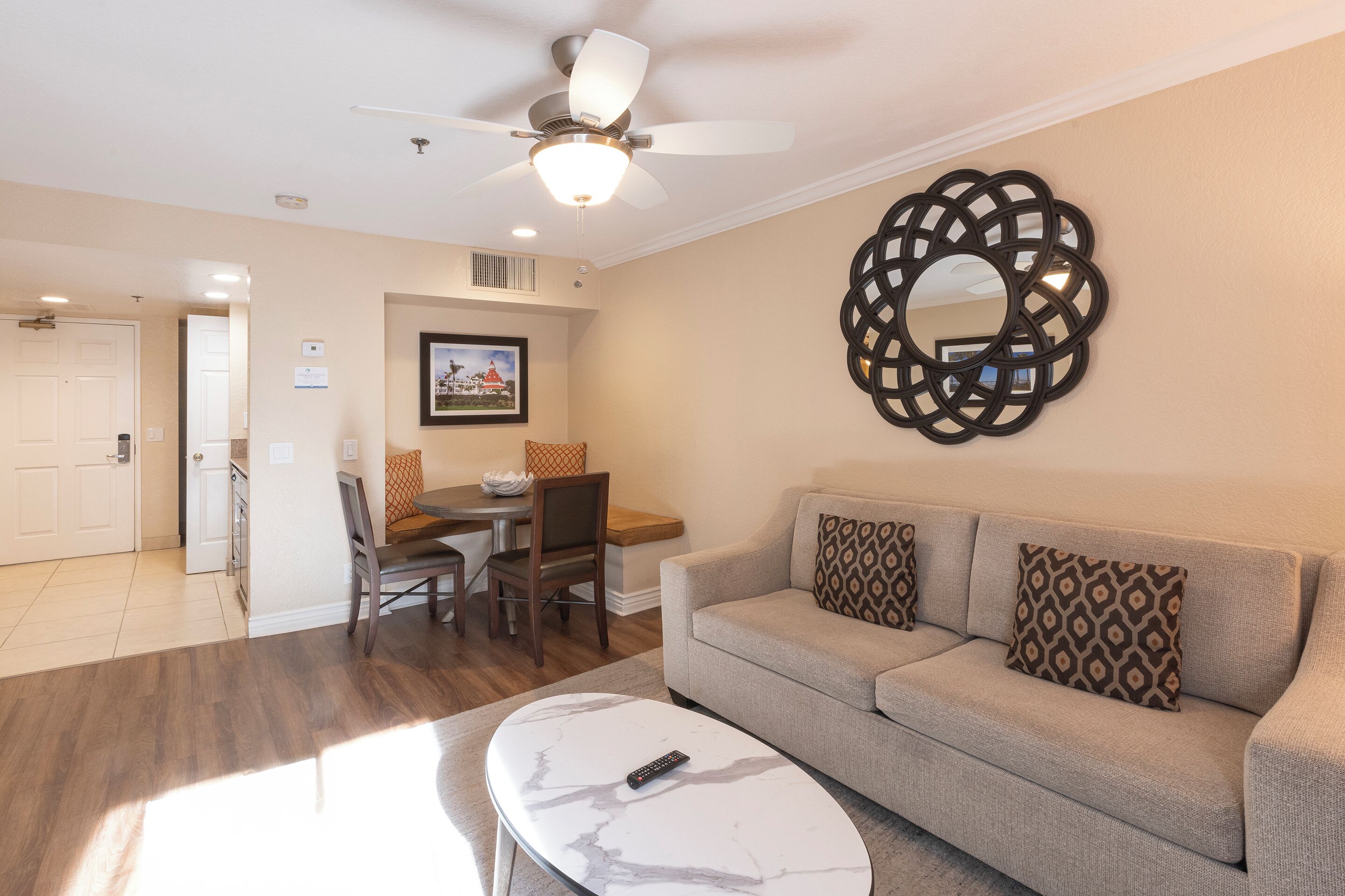 A living room with a sofa, coffee table, and a ceiling fan. There is a dining area with chairs and a table.