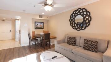 A living room with a sofa, coffee table, and a ceiling fan. There is a dining area with chairs and a table.