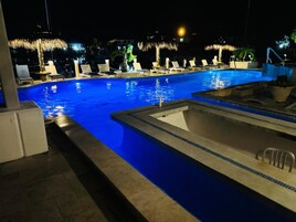 Una piscina nocturna con sillones de descanso y palmeras.