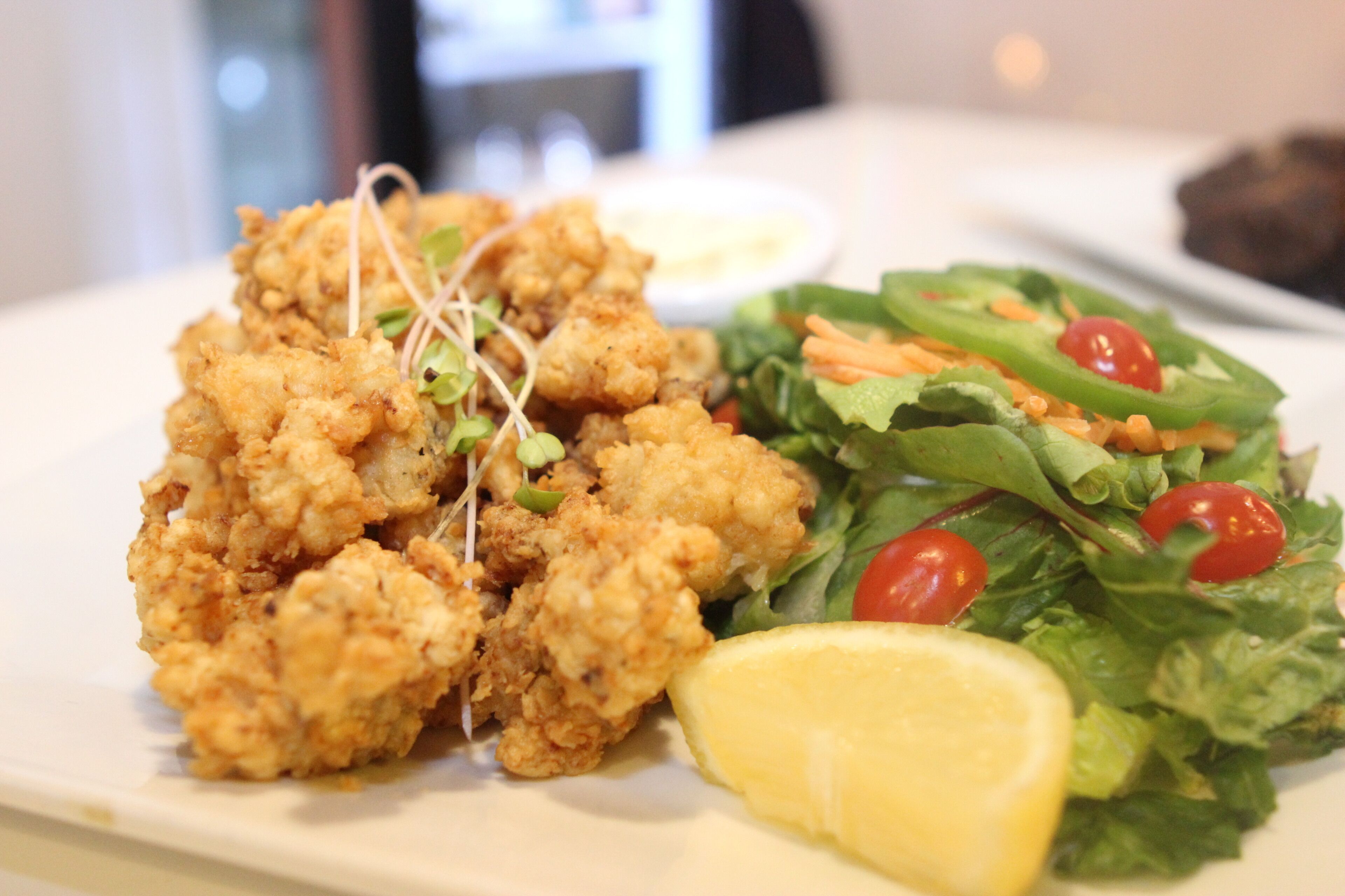 A plate of fried chicken with a side salad and a lemon wedge.