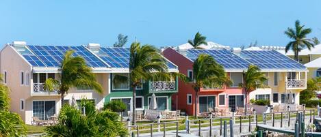 A row of colorful buildings with solar panels, palm trees, and a dock.