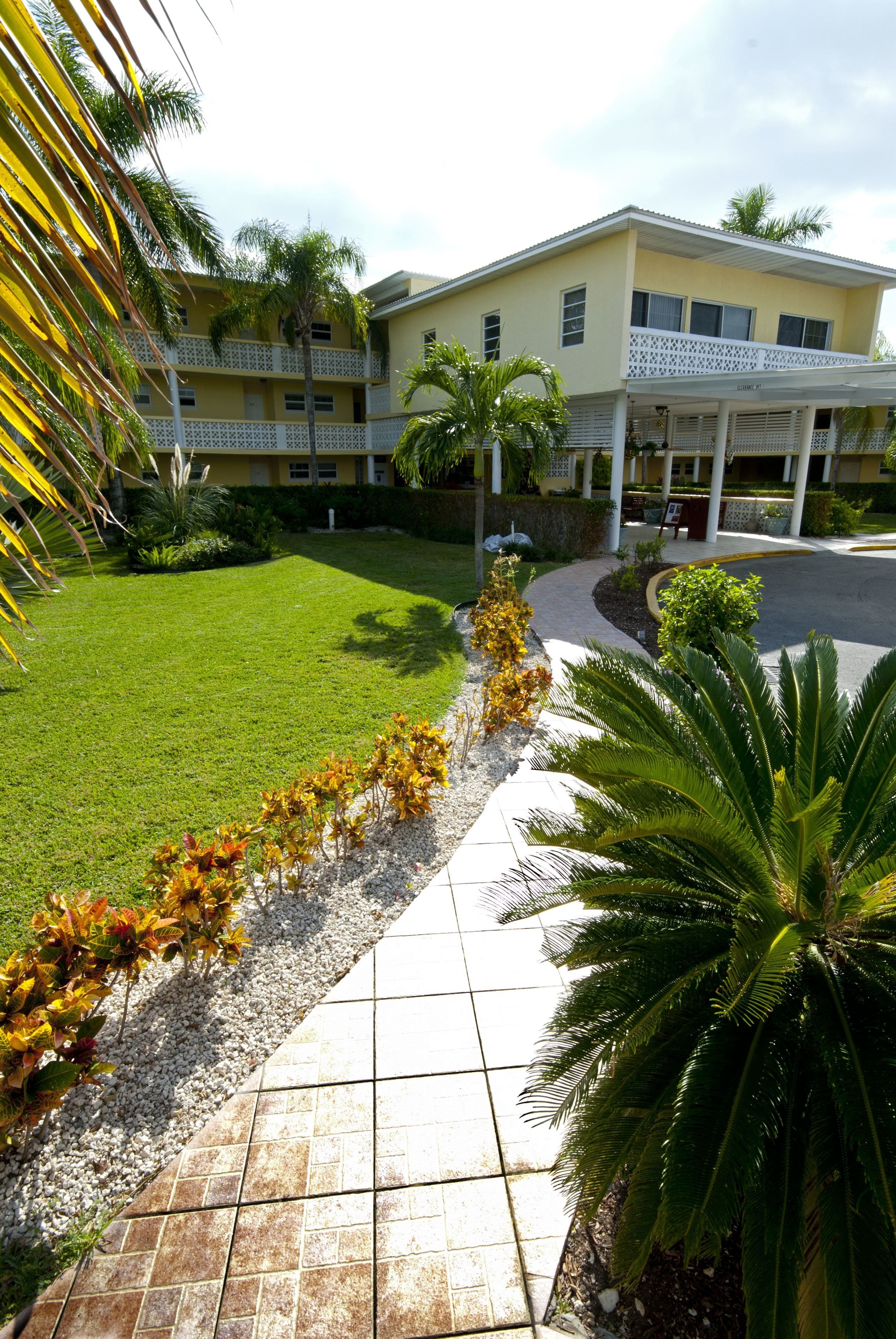A hotel with a well-maintained lawn, a tiled walkway, and a building with a balcony.