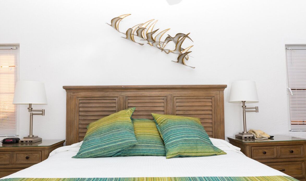 A neatly made bed with two pillows, a wooden headboard, bedside lamps, and a wall-mounted decorative piece.